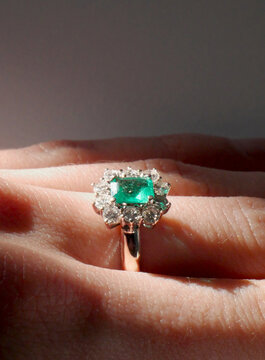 close up of an emerald engagement ring on a woman's hand lit by a light beam