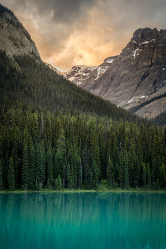 View into land across Emerald Lake of a forest and mountain landscape at sunrise, Yoho National Park, British Columbia, Canada 