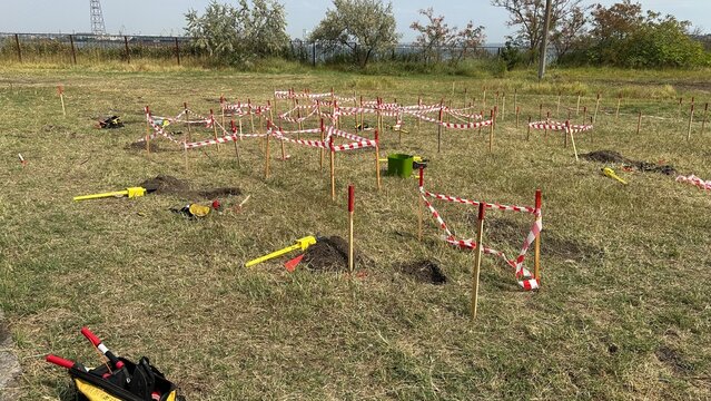 Marked area for humanitarian demining operations in Ukraine. Wooden stakes and red-white warning tape mark a suspected hazardous area where explosive ordnance disposal specialists are working to locat