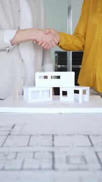 Business partners shaking hands over architectural model, finalizing real estate deal during office meeting. Architecture and business concept