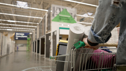 Person pushing a shopping cart with wallpaper rolls in a home improvement store © Ruslan