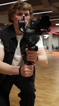 Vertical screen focused videographer carefully filming with handheld gimbal camera in modern studio concentrating on shot composition steady motion and professional workflow in creative space