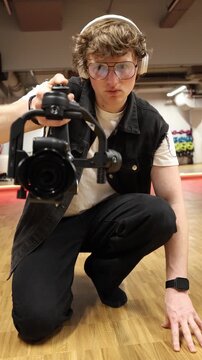 Vertical screen beginner videographer kneeling low holding camera on stabilizer capturing dynamic low angle shot learning movement control focusing on framing and improving shooting skills