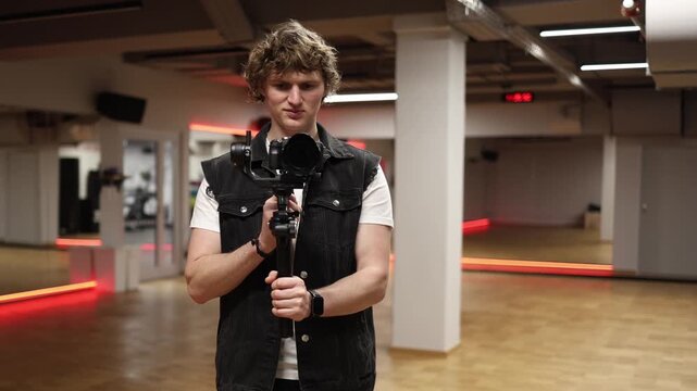 Cameraman stands holding camera on gimbal stabilizer facing forward looking straight and recording video with steady hands using professional filming equipment