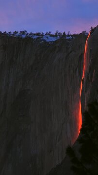 Vertical Screen: Yosemite National Park Firefall phenomenon where sunset illuminates Horsetail Fall creating glowing orange lava-like cascade down granite cliff face at twilight