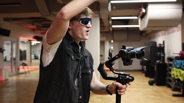 Young videographer dances energetically while holding camera on stabilizer in studio creative filming process showing dynamic movement playful shooting style and active content