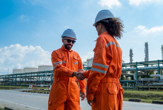 Professional male female engineer  jumpsuit shak hand front oil refinery infrastructure representing successful business partnership industrial agreement teamwork corporate achievement energy sector