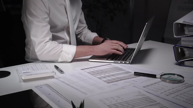 Dedicated finance professional at a cluttered desk, focused on analyzing documents and numbers with laptop, calculator and magnifying glass while managing company records and budgets