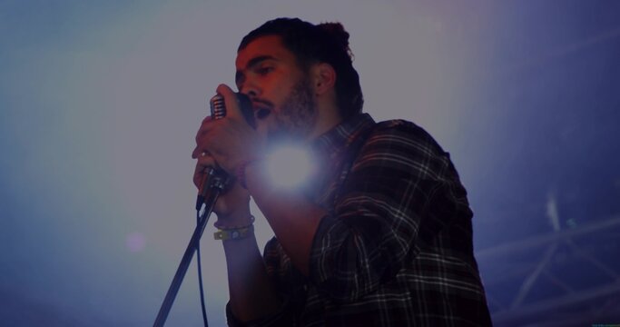 Singing male singer leaning toward vintage microphone on stage, showing plaid shirt and bracelets