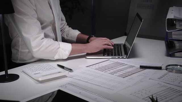 Dedicated finance professional at a cluttered desk, focused on analyzing documents and numbers with laptop, calculator and magnifying glass while managing company records and budgets