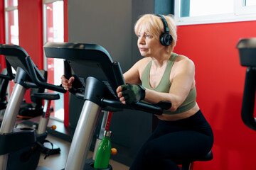 Fototapeta premium Senior woman training on stationary bicycle in gym