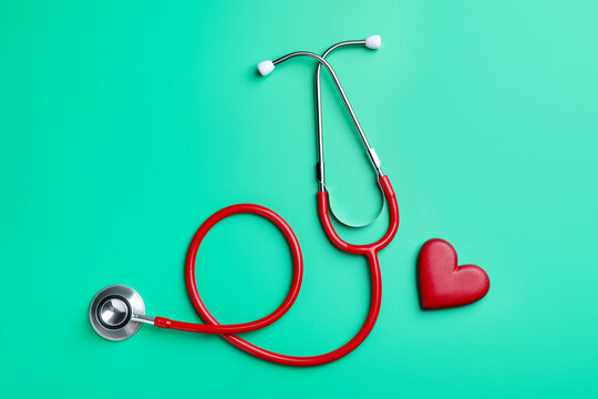 Red stethoscope and heart model on green background, flat lay