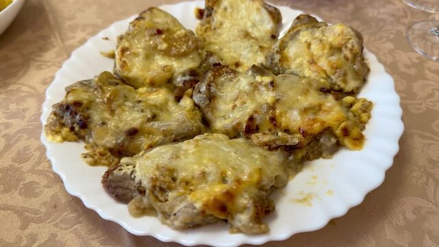 White plate pork with melted cheese, French holiday comfort meal captured closeup on patterned tablecloth. Sliced pork cutlets.