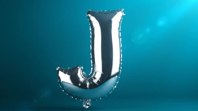 Silver metallic letter J foil balloon floating against a teal blue studio background with studio lighting