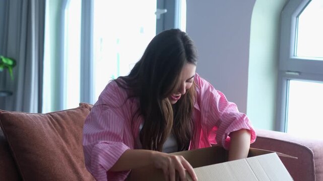 A joyful woman receives and opens a delivery package with excitement. She discovers a new product inside, expressing happiness and satisfaction with her online shopping purchase.