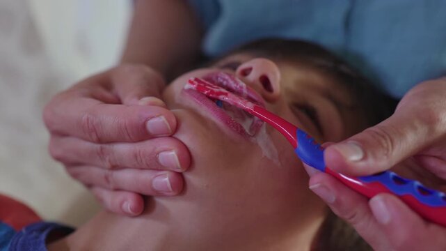 Mother carefully brushing young boy&rsquo;s teeth while he leans back trusting parenting moment of patience guidance and everyday hygiene routine at home