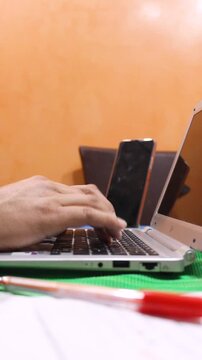The hands of an unrecognizable person are typing on a laptop keyboard on a table inside a house. Concept of remote work and technology