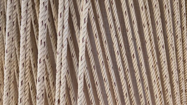 Vertical twisted rope texture. Vertical cream-colored twisted rope texture. Close-up of a woven rope curtain. Rustic home decor aesthetic with warm tones and soft organic lines.