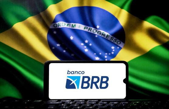 BRB Bank logo on a smartphone screen with the Brazilian flag in the background. Moody's cuts credit rating and downgrades BRB to high risk of default.