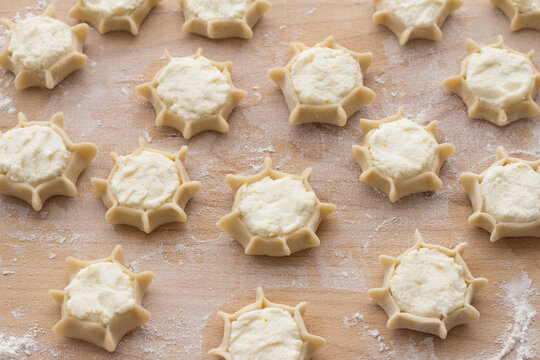 Many raw Italian cheese cookies with lemon zest filling prepared on a floured surface. Traditional Sardinian pardulas pastry production at home
