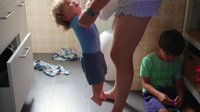 Toddler standing in kitchen pulling on caregiver clothing seeking attention and closeness emotional childhood moment of need and connection during everyday routine