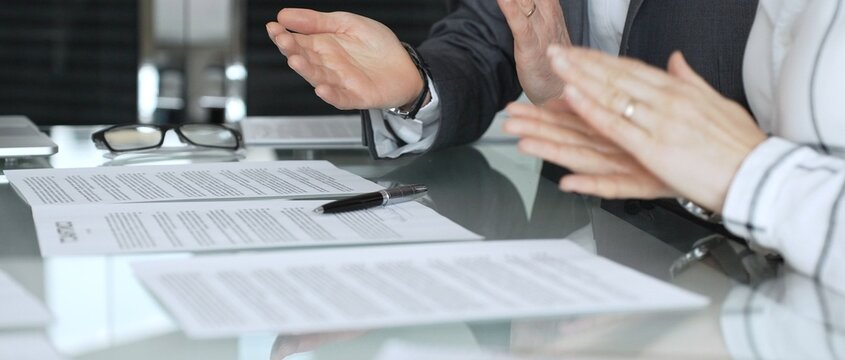 Businessman signing contract documents while female colleague is clapping, finalizing successful partnership agreement. Business people concept