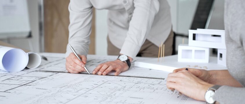Architects are discussing building plans, using a compass over blueprints while collaborating on a new construction project in an office, emphasizing design, planning, and teamwork, close up