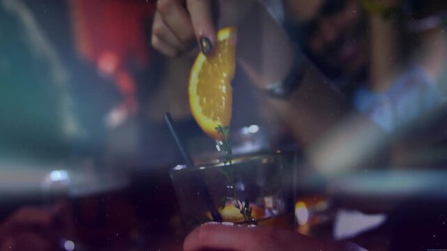 Woman's hand reaching adjusting herb and placing orange wedge as man holding cocktail, bar prep