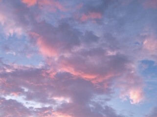 Fototapeta premium Dramatic twilight sky filled with voluminous cumulus clouds glowing in soft pastel hues of pink, magenta, lavender, and purple.