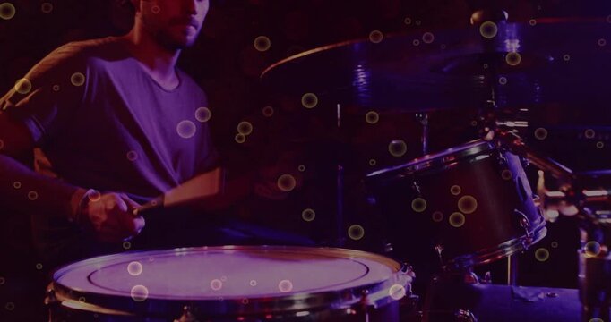 Drummer raising sticks playing drum part under lights after music cue while bokeh over kit floating