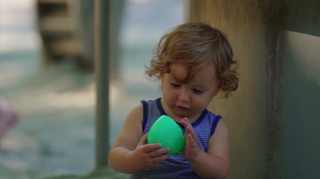 Toddler examining small toy with focused attention in sandbox becoming absorbed in exploration before sibling interrupts and takes object capturing curiosity and interaction