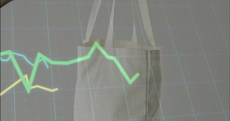Obraz premium Hanging seamed beige tote with straps in studio, overlaying green-cyan-yellow line graphs on grid