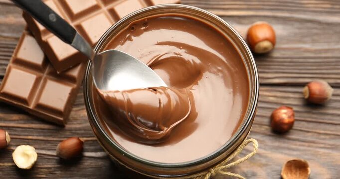 Woman taking tasty chocolate paste with spoon from jar at wooden table, closeup