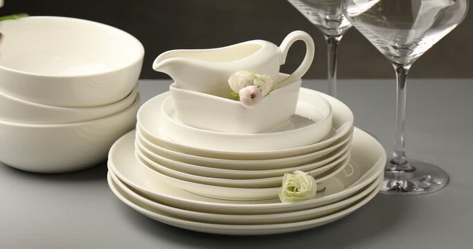 Woman stacking clean dishware and putting beautiful flowers at grey table, closeup