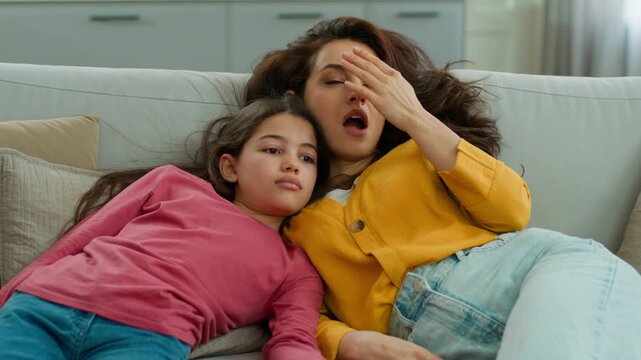 Tired Caucasian family falling on sofa sleepy woman mom little girl child sister exhausted kid mother jumping on couch female daughter resting relaxing hard day cleaning at home apartment living room