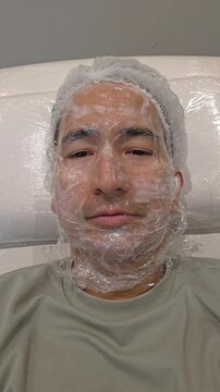 Treatment, cure of face skin in dermatology clinic. Scars procedure with problem skin for man. Man with cream with anesthesia and plastic film on his face before laser therapy procedure.