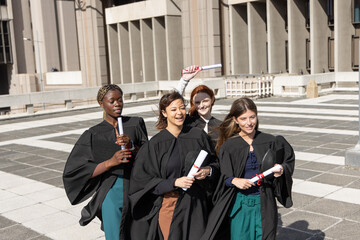 Diverse female graduates walking across campus plaza in gowns, holding diplomas and caps, smiling © wavebreak3