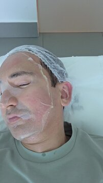 Facial mask of man in dermatologist office. Man on with therapy room. Man lying on bed. Healing clay to relieve laser treatment. Close-up of a man's face. Vertical.