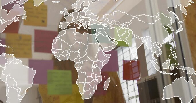 Woman placing sticky notes on glass panel, causing world map overlay while reviewing business plan