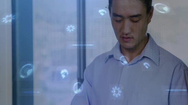 Tapping businessman wearing light shirt using tablet by window, showing blue holographic interface