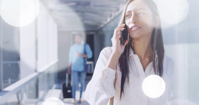 Woman walking airport, talking on phone with suitcase, bokeh glow growing, camera closing to smile
