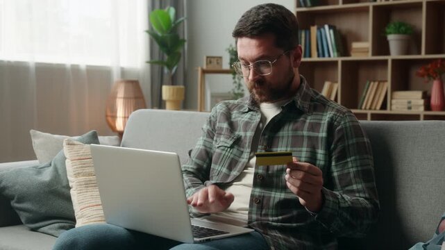 Irritated Caucasian man shopping laptop online credit card transaction problem adult male guy at home couch payment buying internet money e-commerce using computer failure unsuccessful purchase error