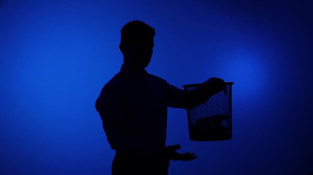 Man in silhouette disposing of crumpled paper into a waste bin against a vibrant blue background, illustrating concepts of waste management, cleaning, and decluttering