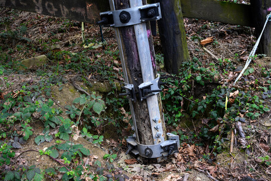 Galvanized iron pole splint, reinforcing metal with collar clamps on old wooden train trestle structural support beams, maintenance and repair patch for added stability and safety
