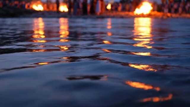 Serene close-up of warm fire reflections dancing on the rippling blue water of the ganges river during ganga dussehra.