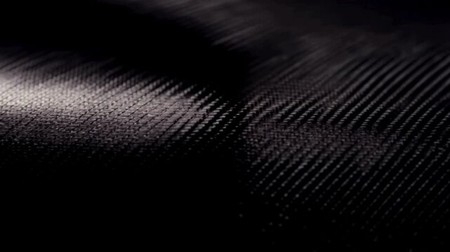 A detailed close up macro shot of black carbon fiber material with light moving across the woven texture. Ideal for automotive or tech themes.
