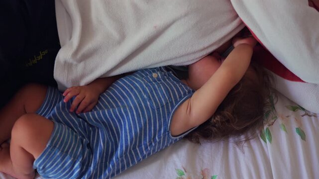 Toddler lying beside sleeping mother reaching arm across her chest showing tender family closeness and quiet moment of childhood comfort in home bedroom