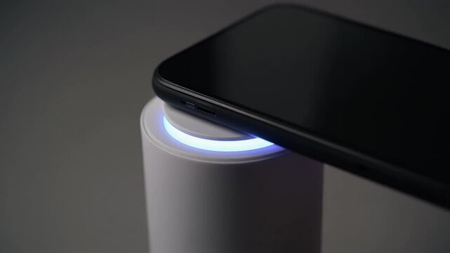 A smartphone wirelessly charges on a sleek white charging pad with blue led light.