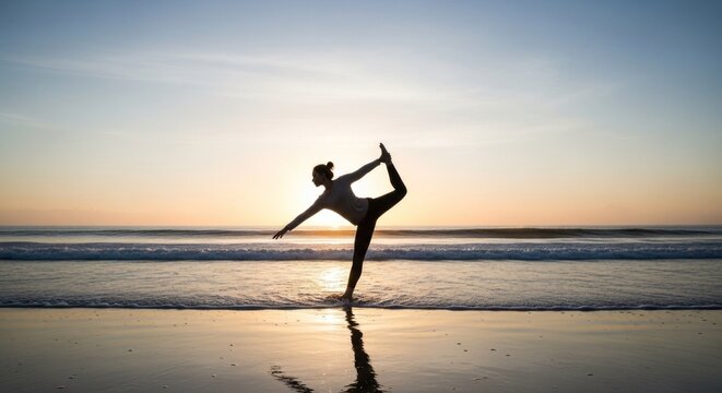 A woman in a black tank top and leggings performs a yoga pose on a sandy beach at sunset.