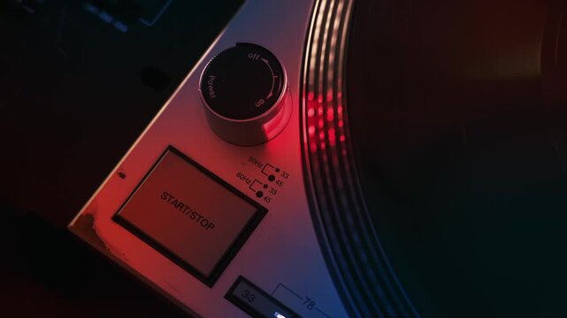 Finger pressing start stop button on vintage turntable, platter spinning with red and blue light.